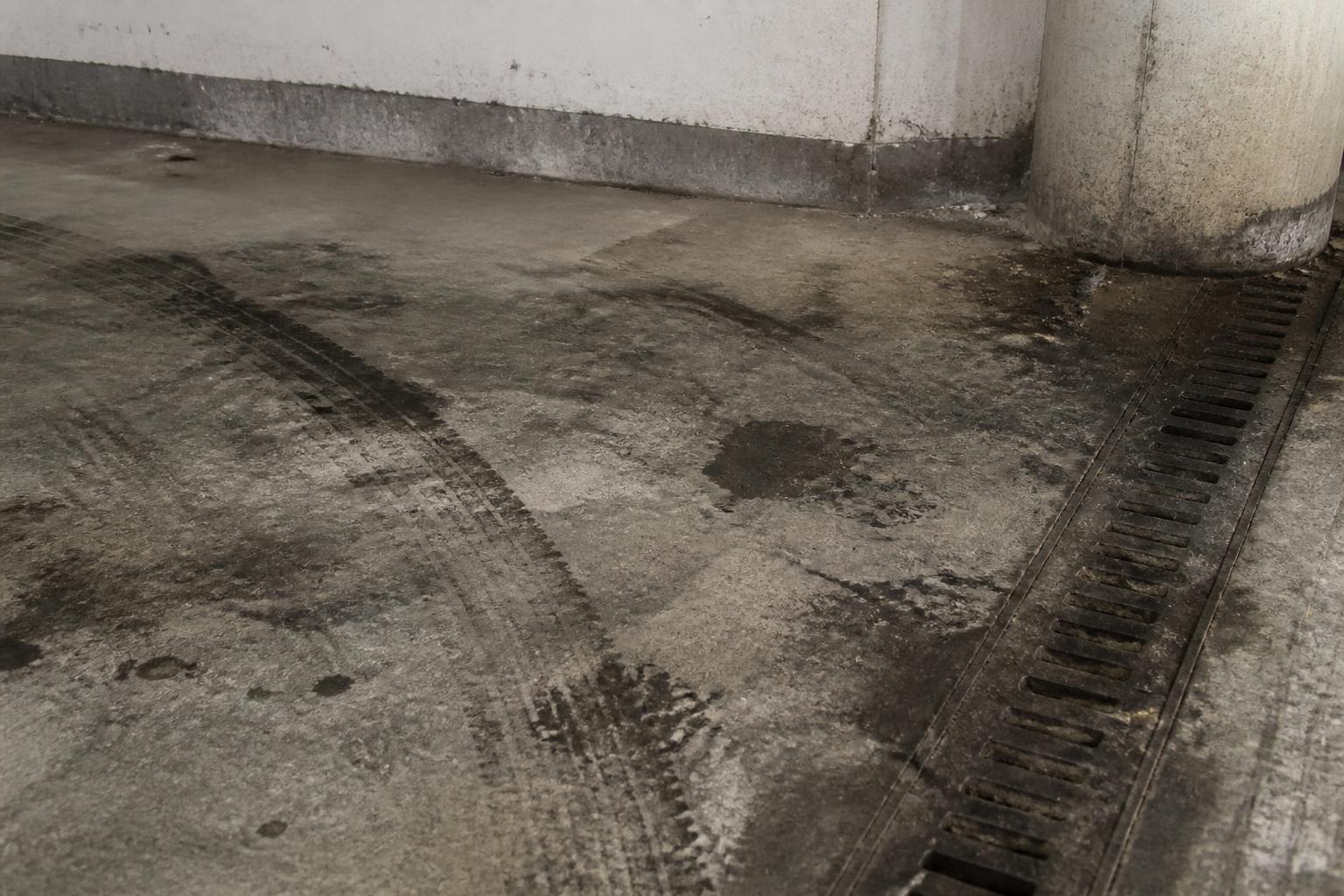 Dirty parking garage concrete floor with tire marks, oil stains and a clogged drainage channel